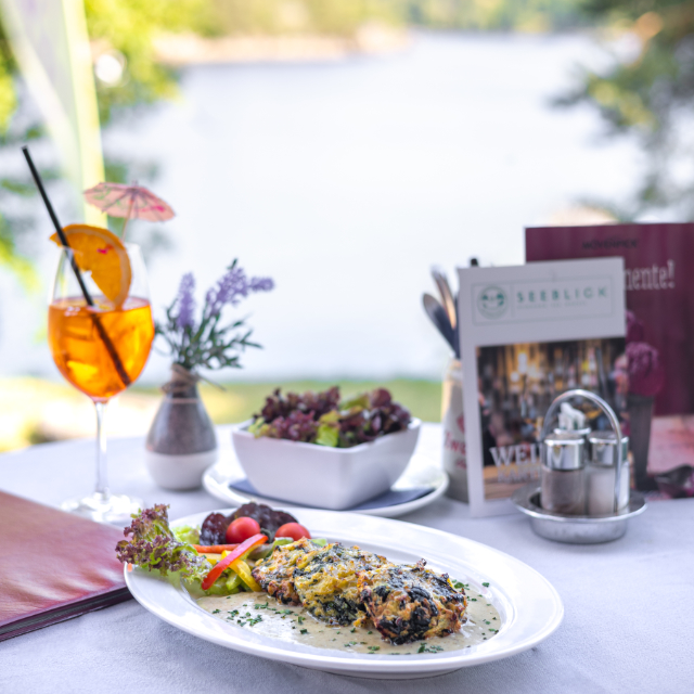 Eine Portion Gemüselaibchen und Glas Aperol Spritz auf dem Tisch mit Seeblick