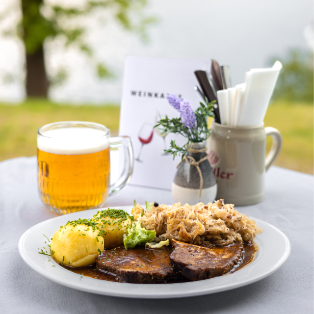 Ein Glas Bier und eine Poriton Fleisch mit Knödel am Tisch draußen